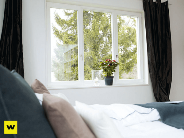 Modernes Schlafzimmer mit gemütlichem Bett, großen Fenstern und Blick ins Grüne.
