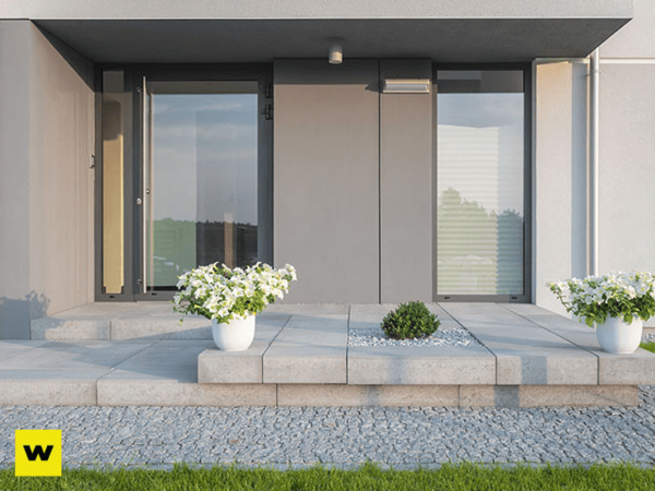 Moderner Hauseingang mit großen Fenstern, Steinplatten und Blumenkübeln im Vorgarten.